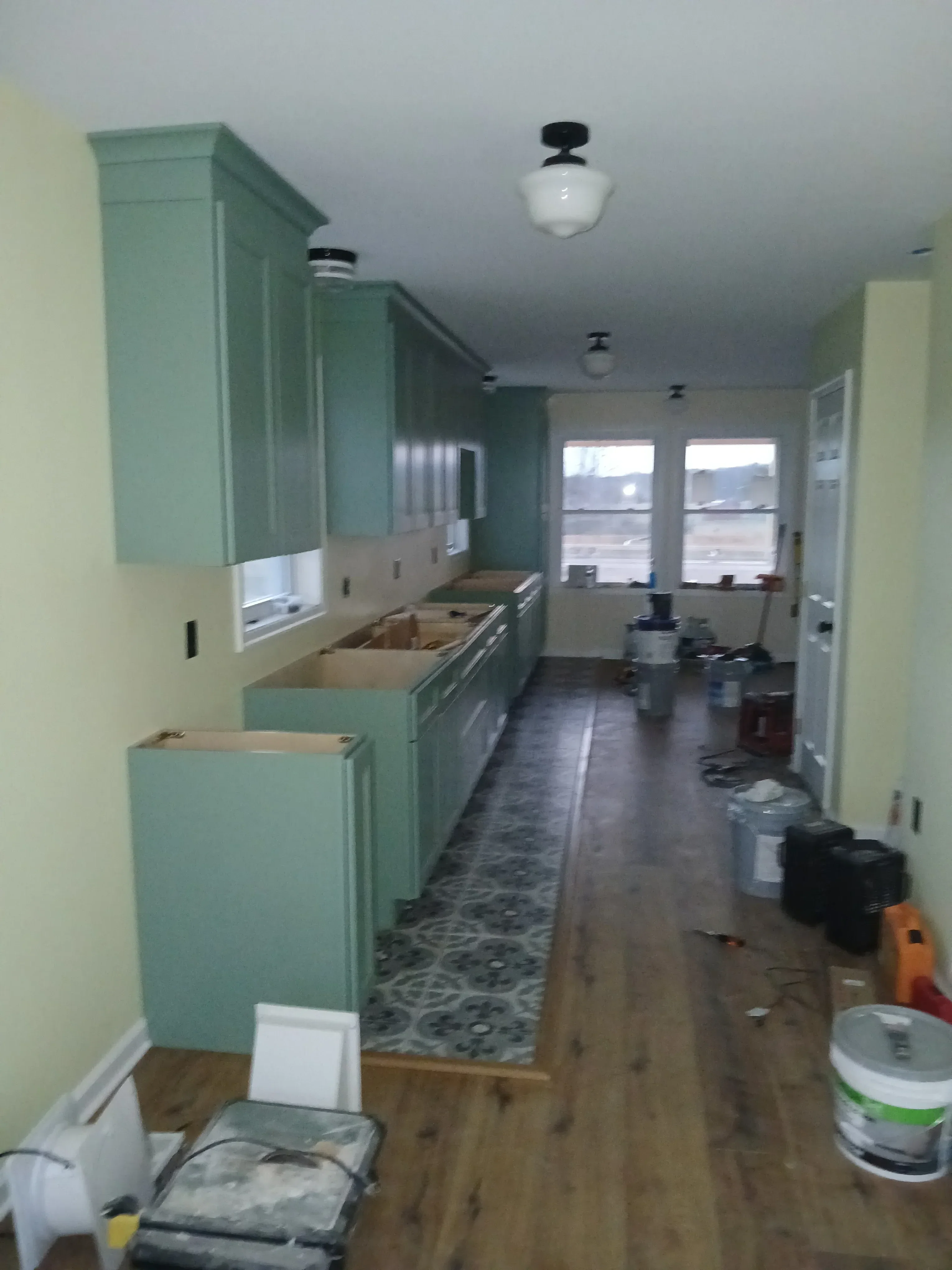 Kitchen renovation with sage green cabinets, drywall, and patterned backsplash tile installation