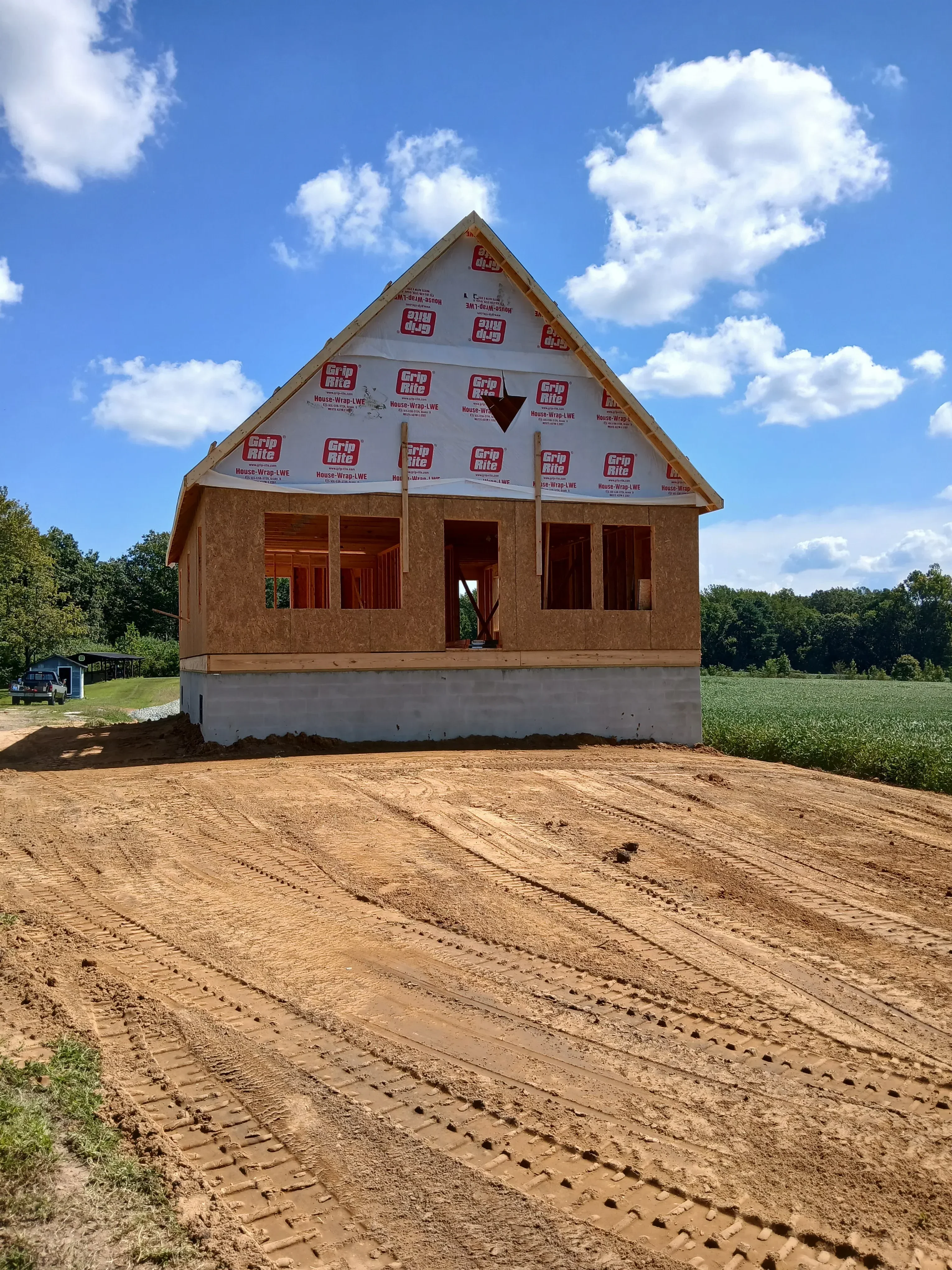Brick home under construction with window openings, concrete foundation, and roof framing