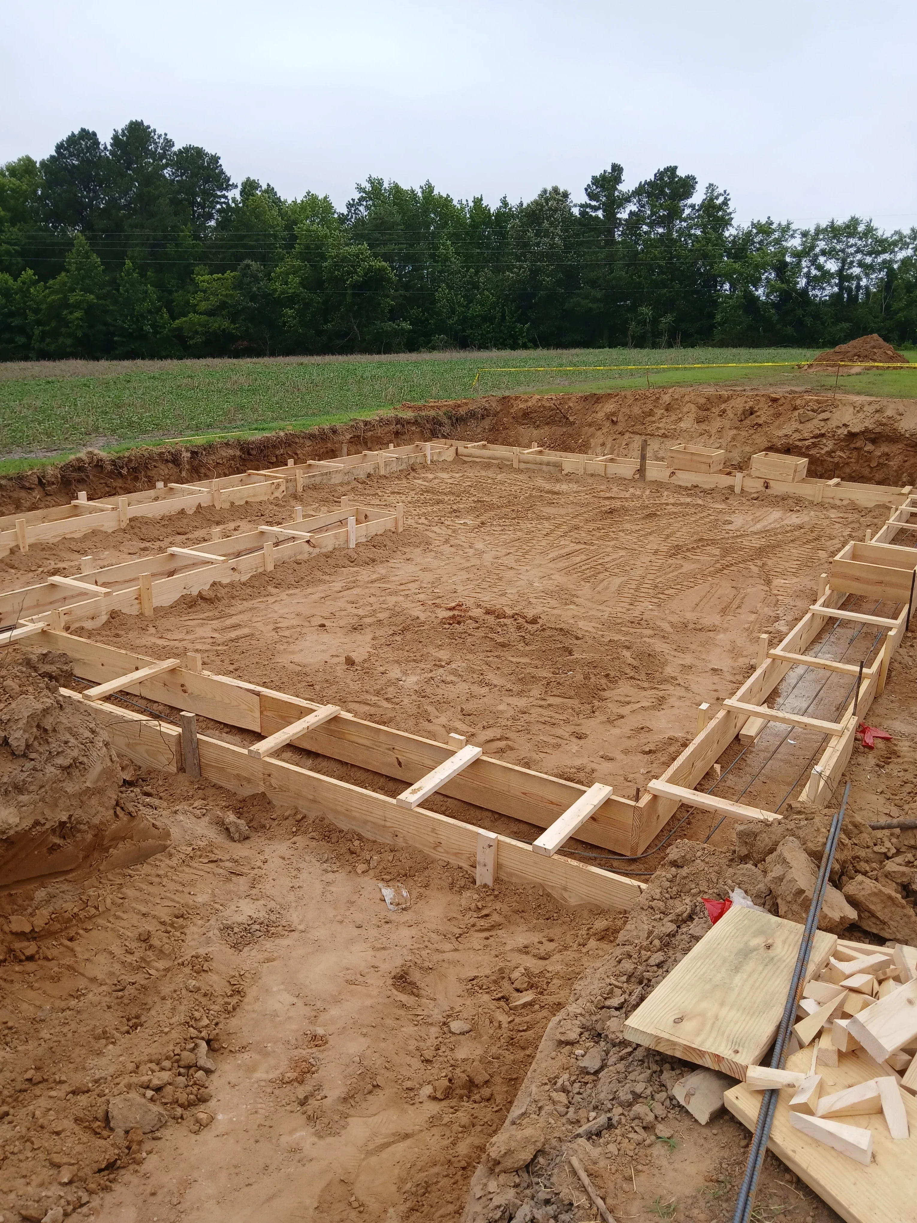 Wooden foundation framing components and materials staged on prepared soil excavation site