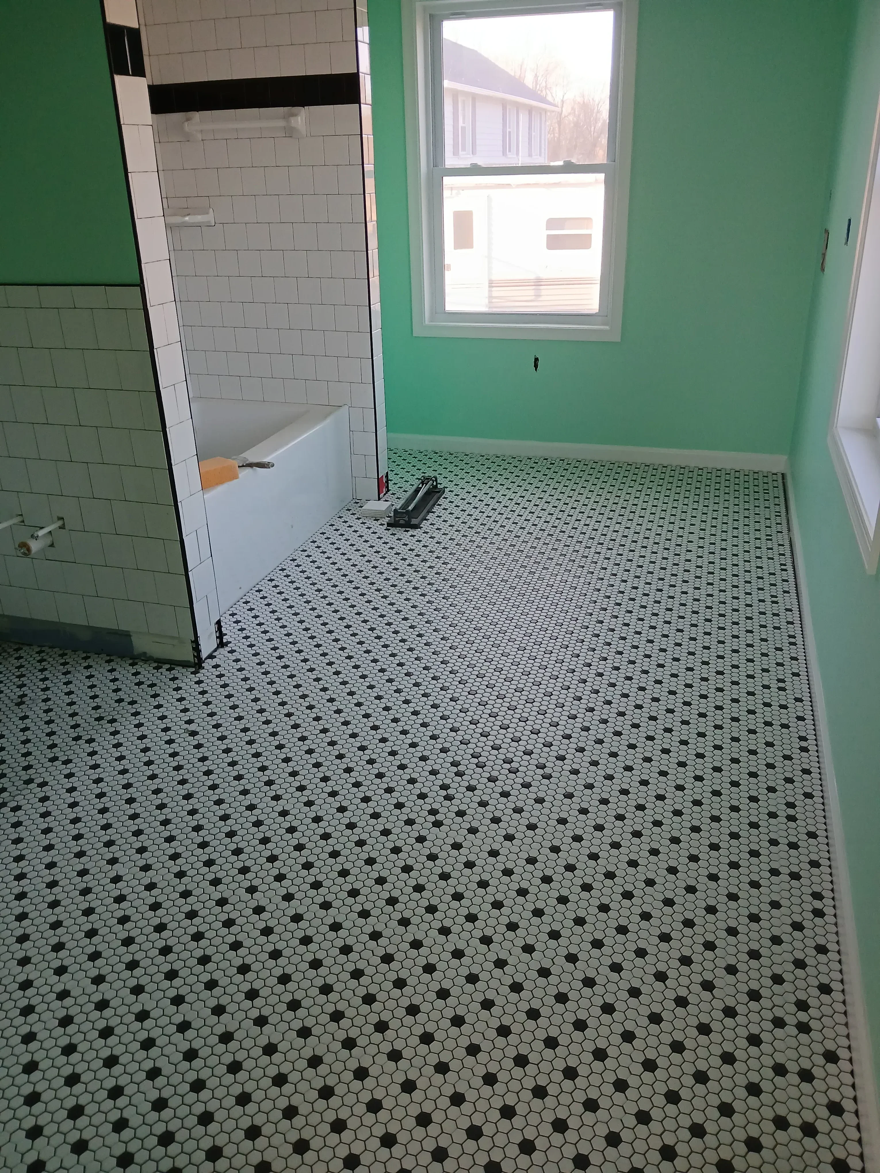 Bathroom with penny round mosaic tile shower wall, white subway tile wainscoting, and green painted walls