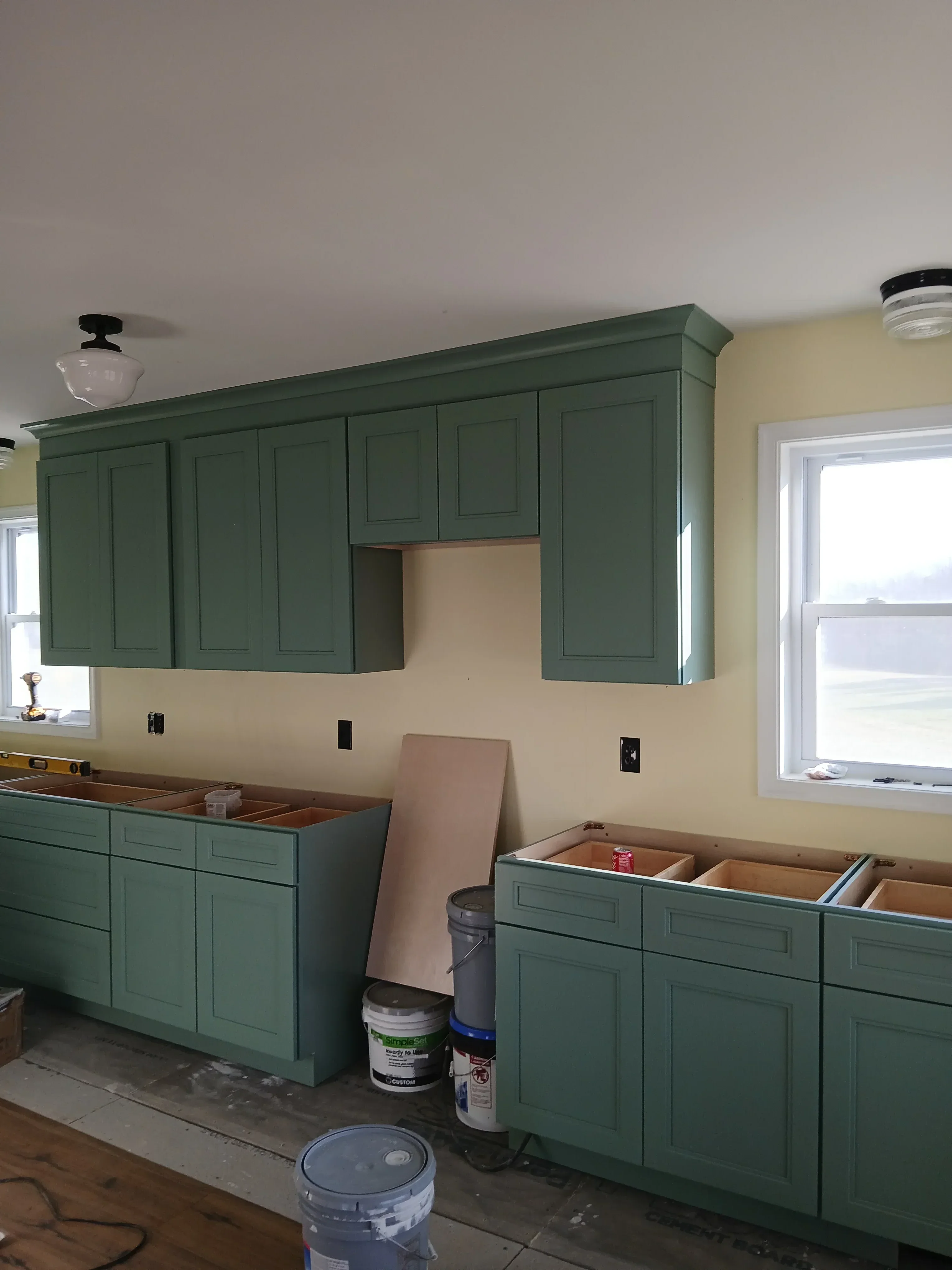 Green recessed panel cabinetry with hardware installed on cream drywall with window above