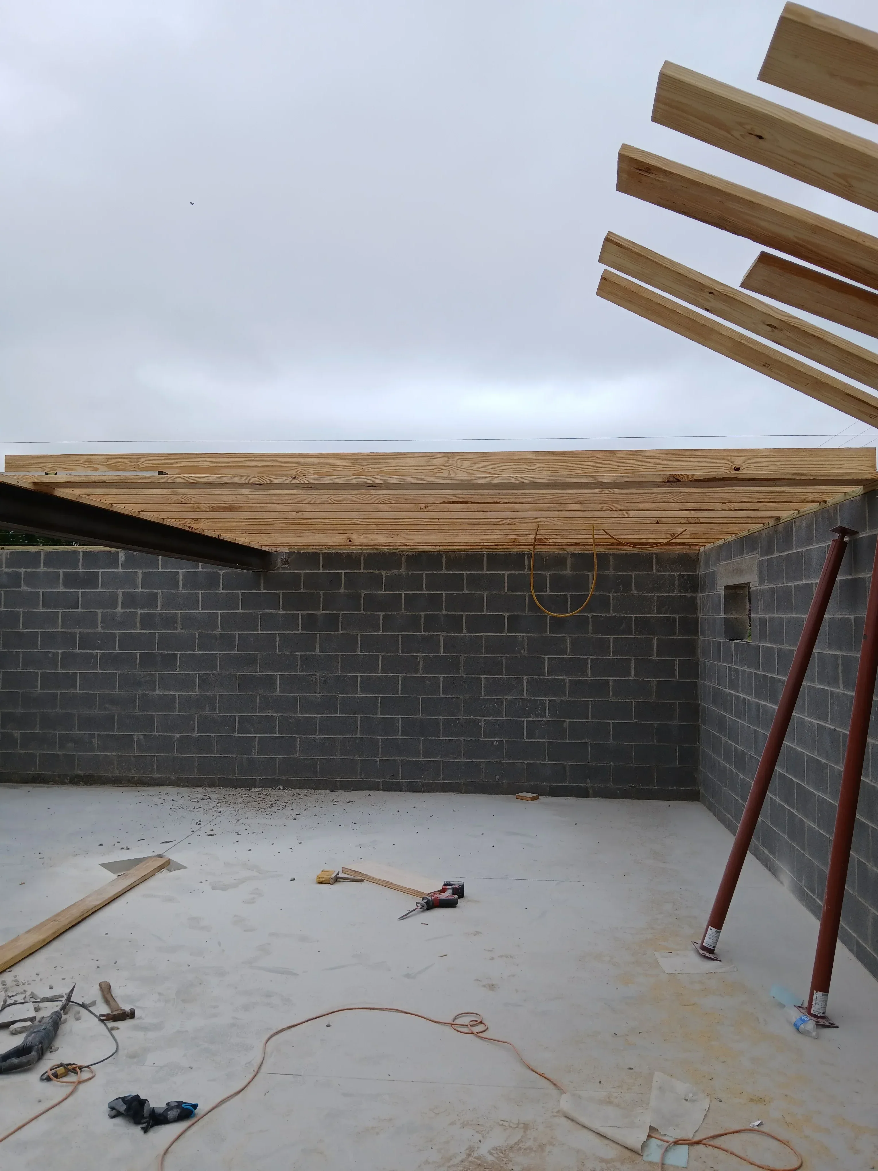 Bathroom with herringbone dark tile floor, wood ceiling framing, and drywall walls under construction