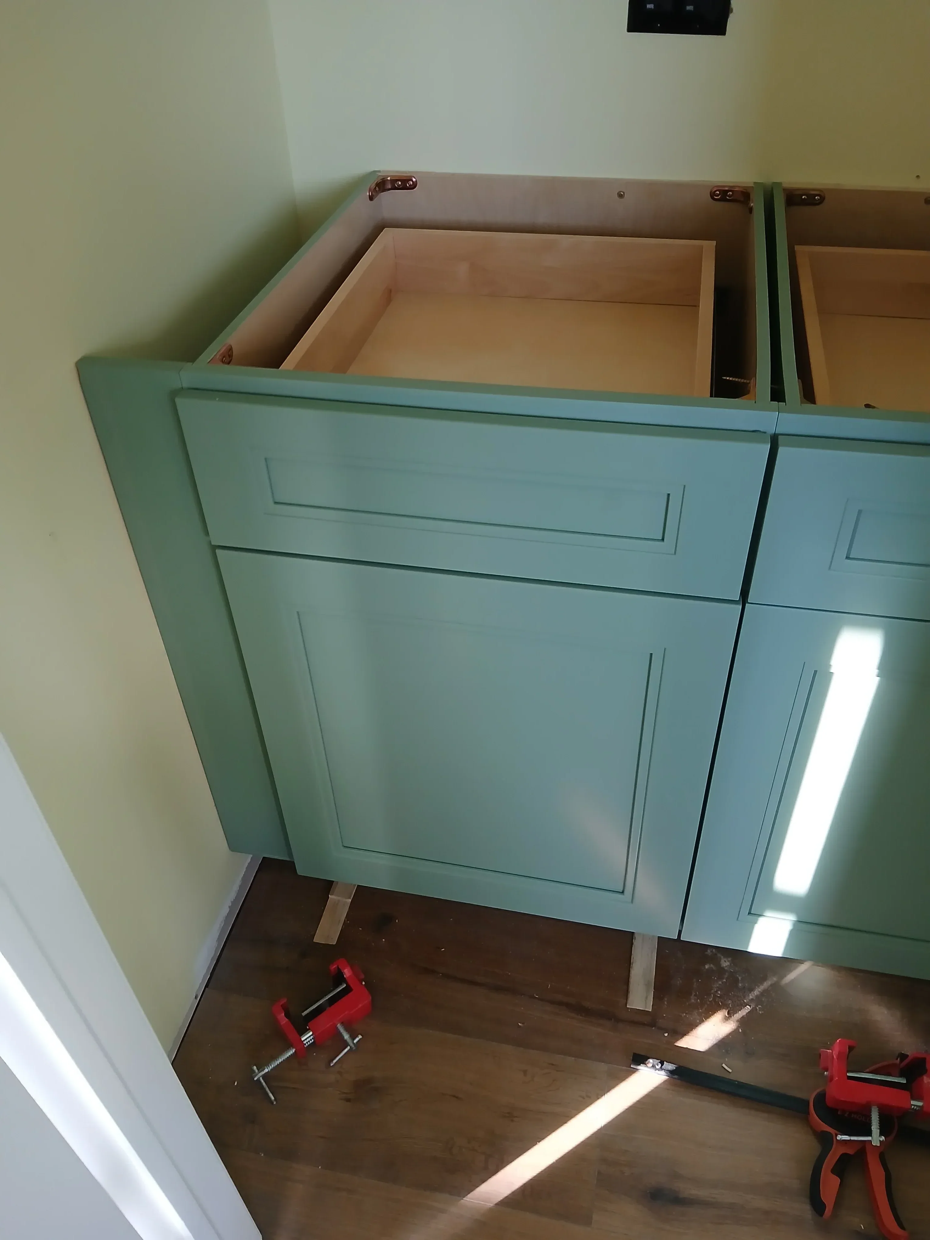 Sage green painted kitchen cabinets with recessed panel doors and brass hardware during installation
