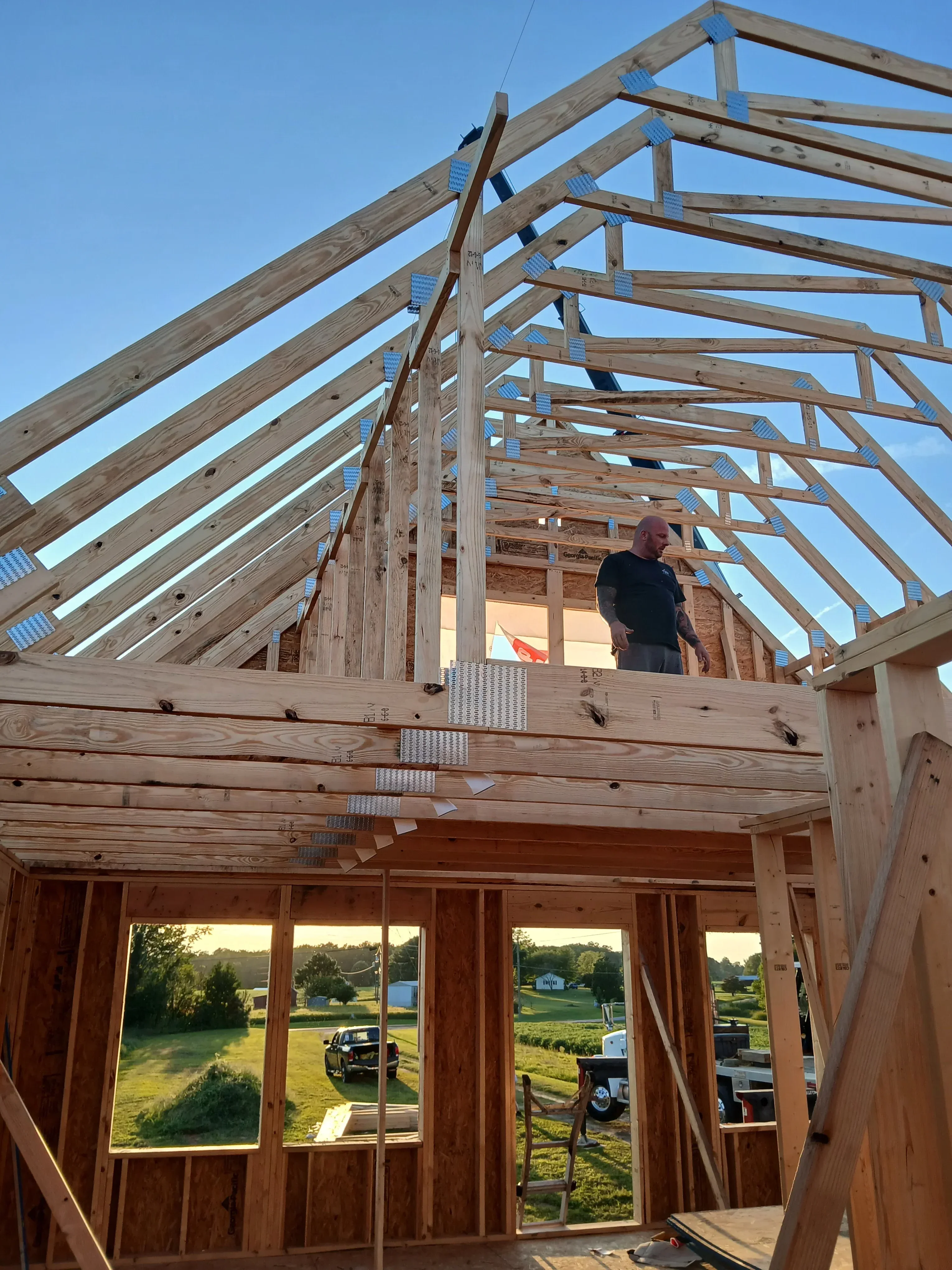 Wood-framed residential structure with roof trusses, metal connectors, and multi-pane windows during construction