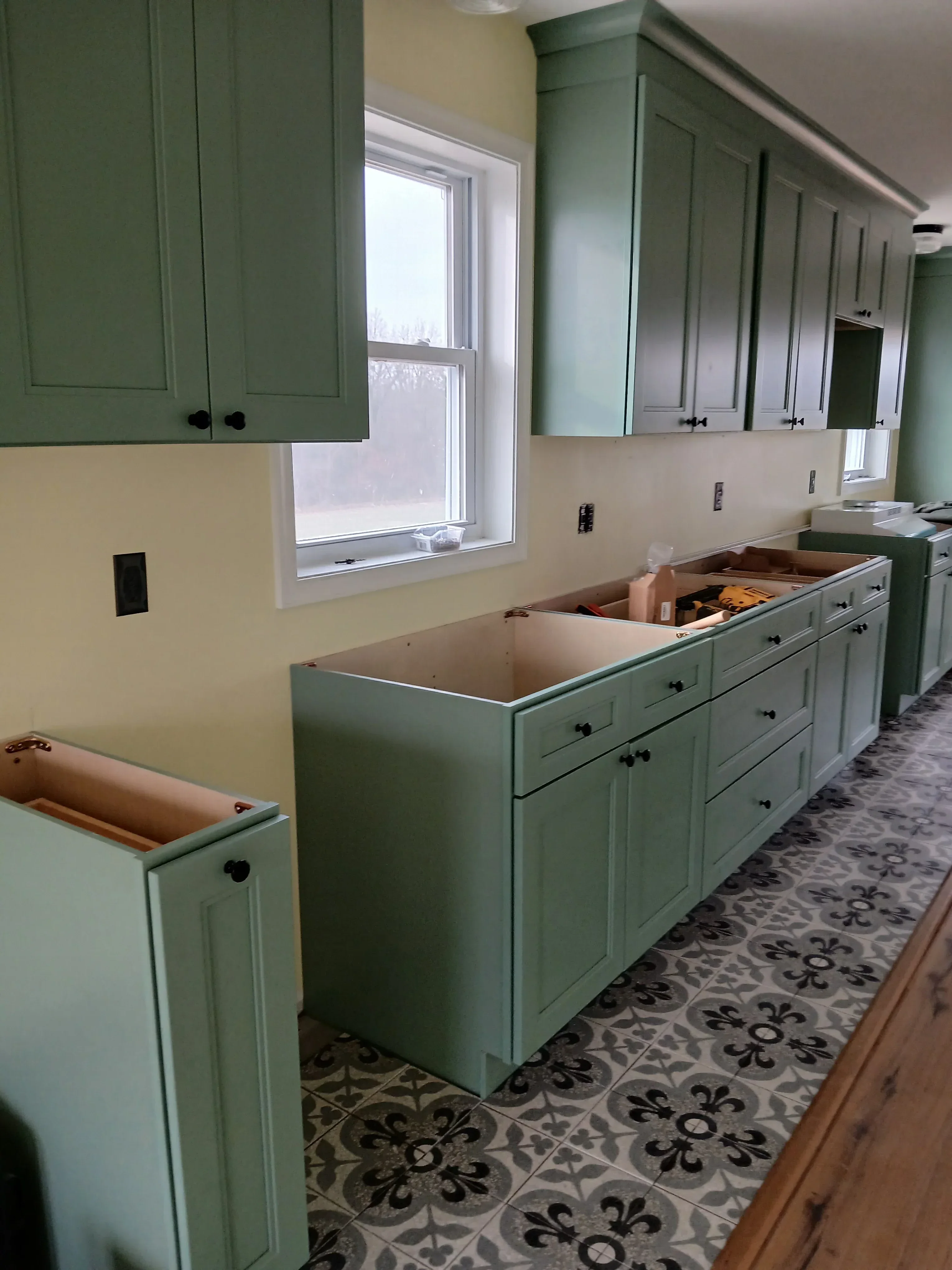 Sage green painted kitchen cabinets with shaker doors and black hardware installed in kitchen space