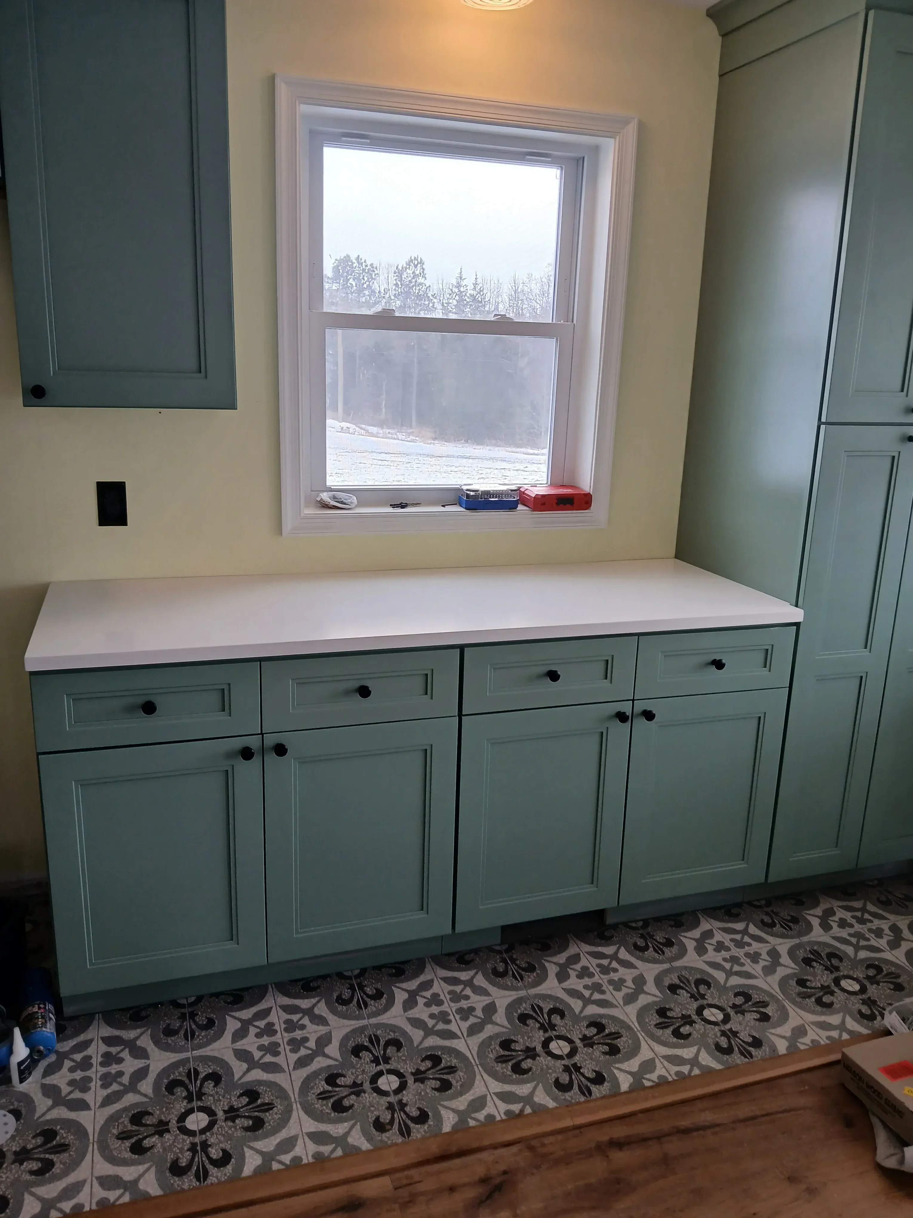 Sage green built-in cabinetry with black hardware and white-trimmed sliding window installation